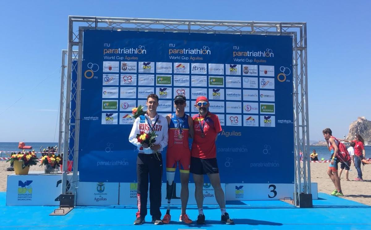 three male Para triathletes on a podium on the beach