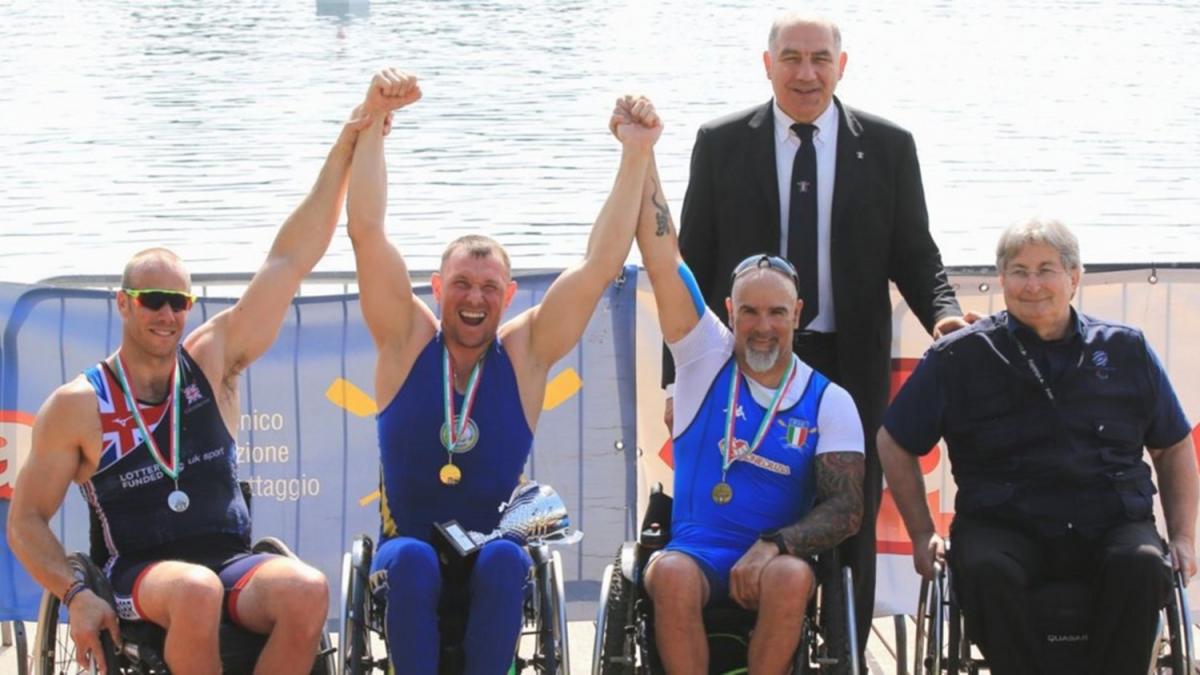 Four persons in wheelchairs and a person behind standing them