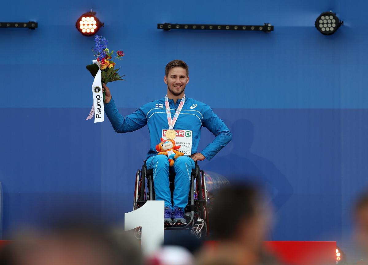 Person in a wheelchair on a podium holding flowers 