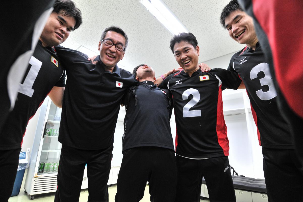 a group of male goalball players standing in a circle laughing 