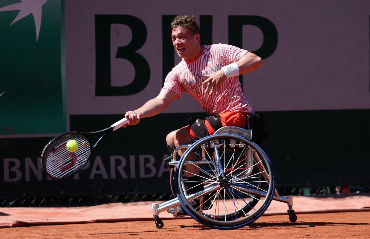 a male wheelchair tennis player reaches for a shot on a clay court