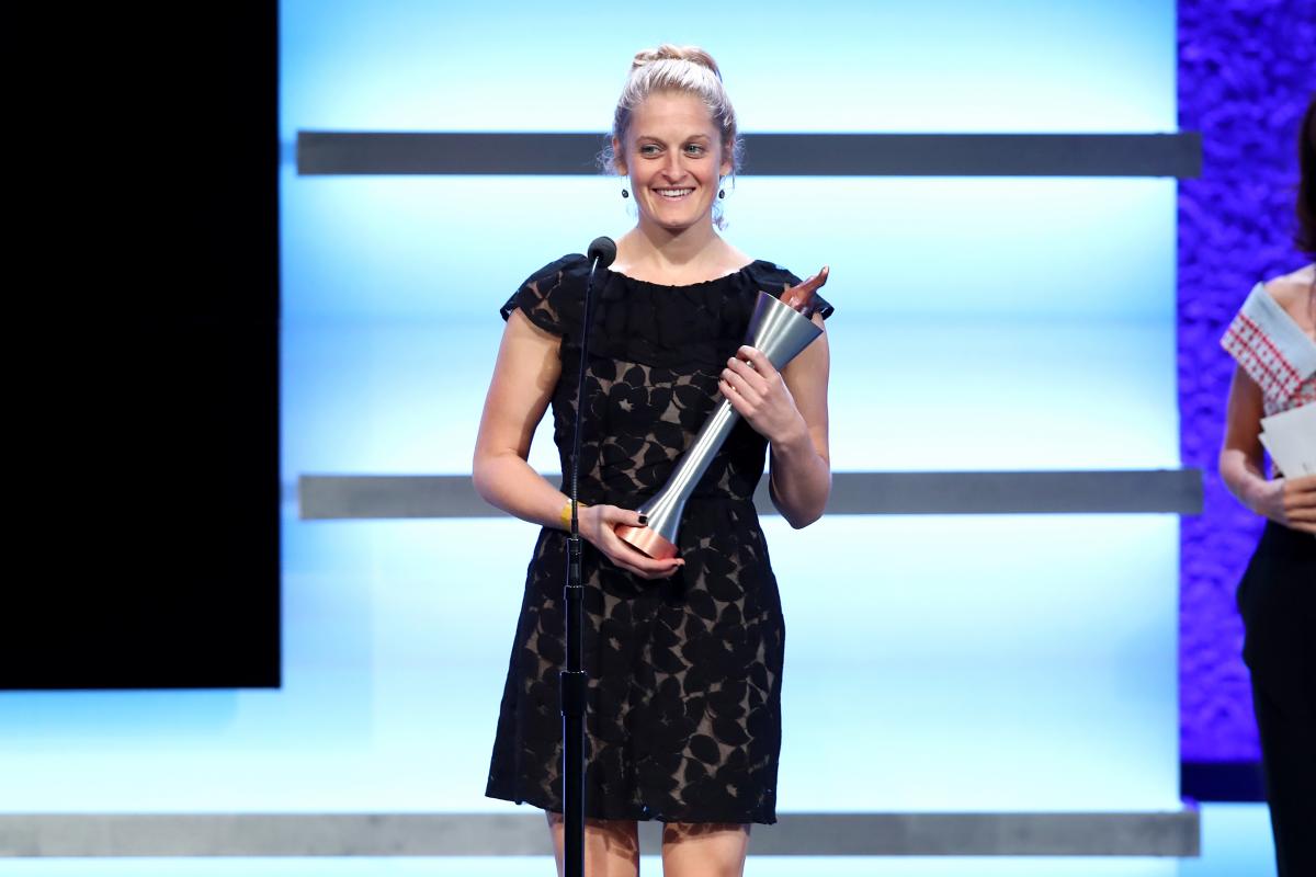 a woman stands on stage holding a trophy