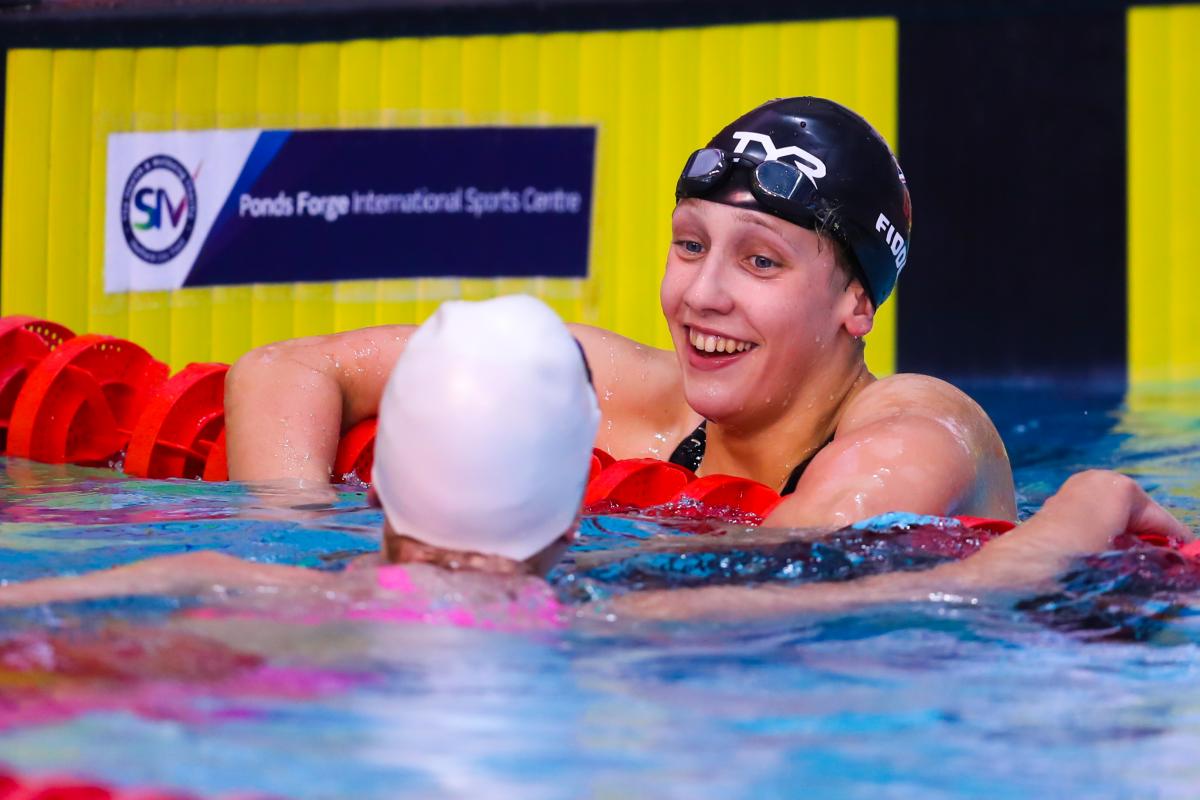 a female Para swimmer leans on the rope and chats to another swimmer