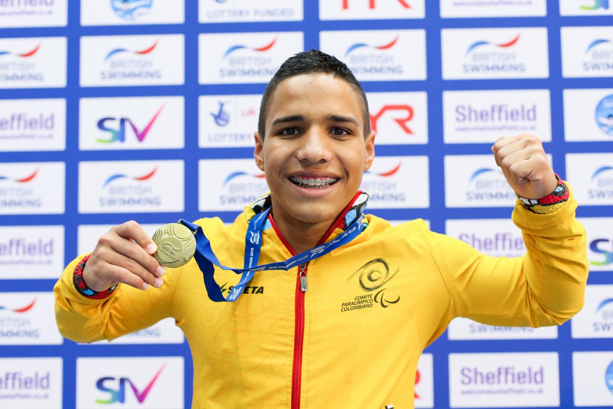 a male Para swimmer holds up his gold medal and smiles