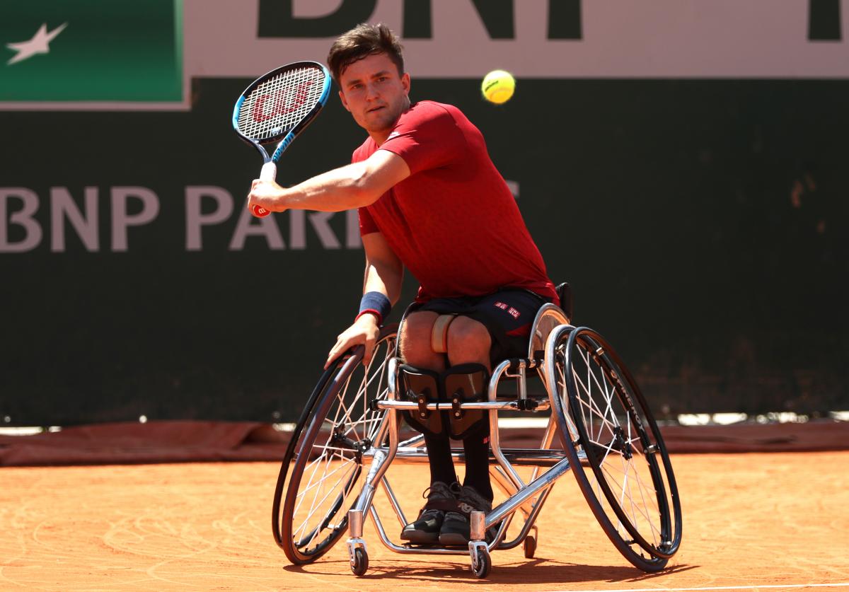 a male wheelchair tennis player plays a backhand on a clay court