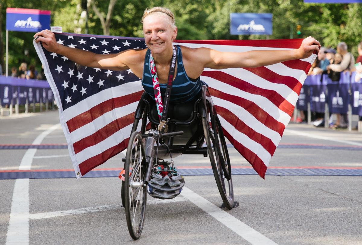 A female wheelchair racer holds up an American flag