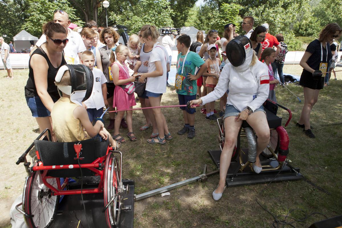 Group of children watching two people practicing wheelchair fencing