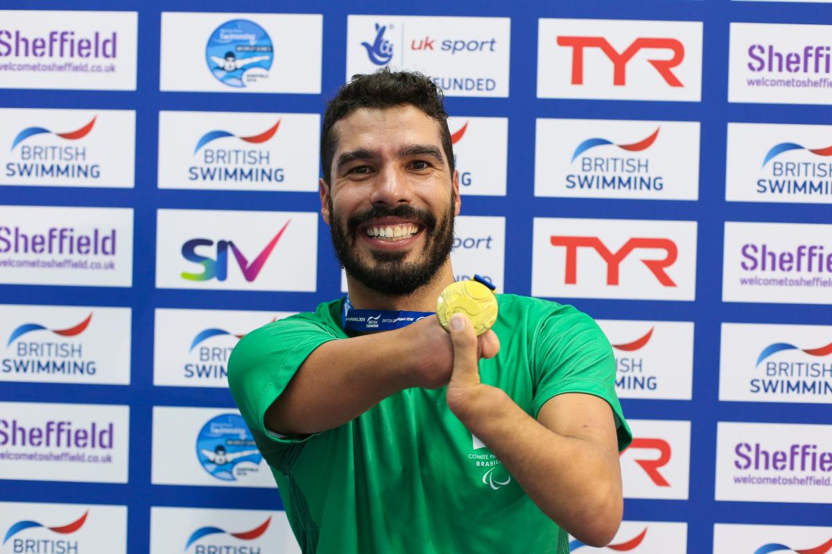 a male Para swimmer smiles and holds up his gold medal