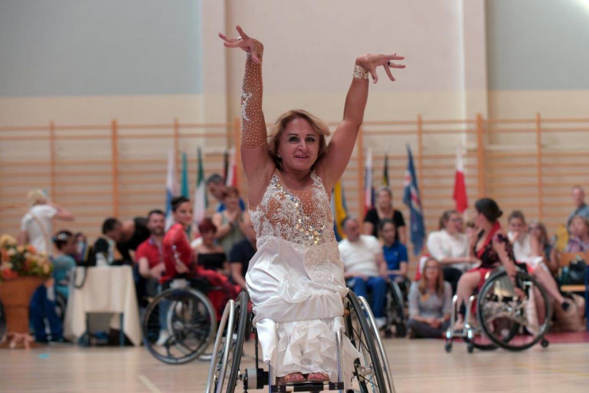 a female wheelchair dancer raises her arms above her head as part of a move