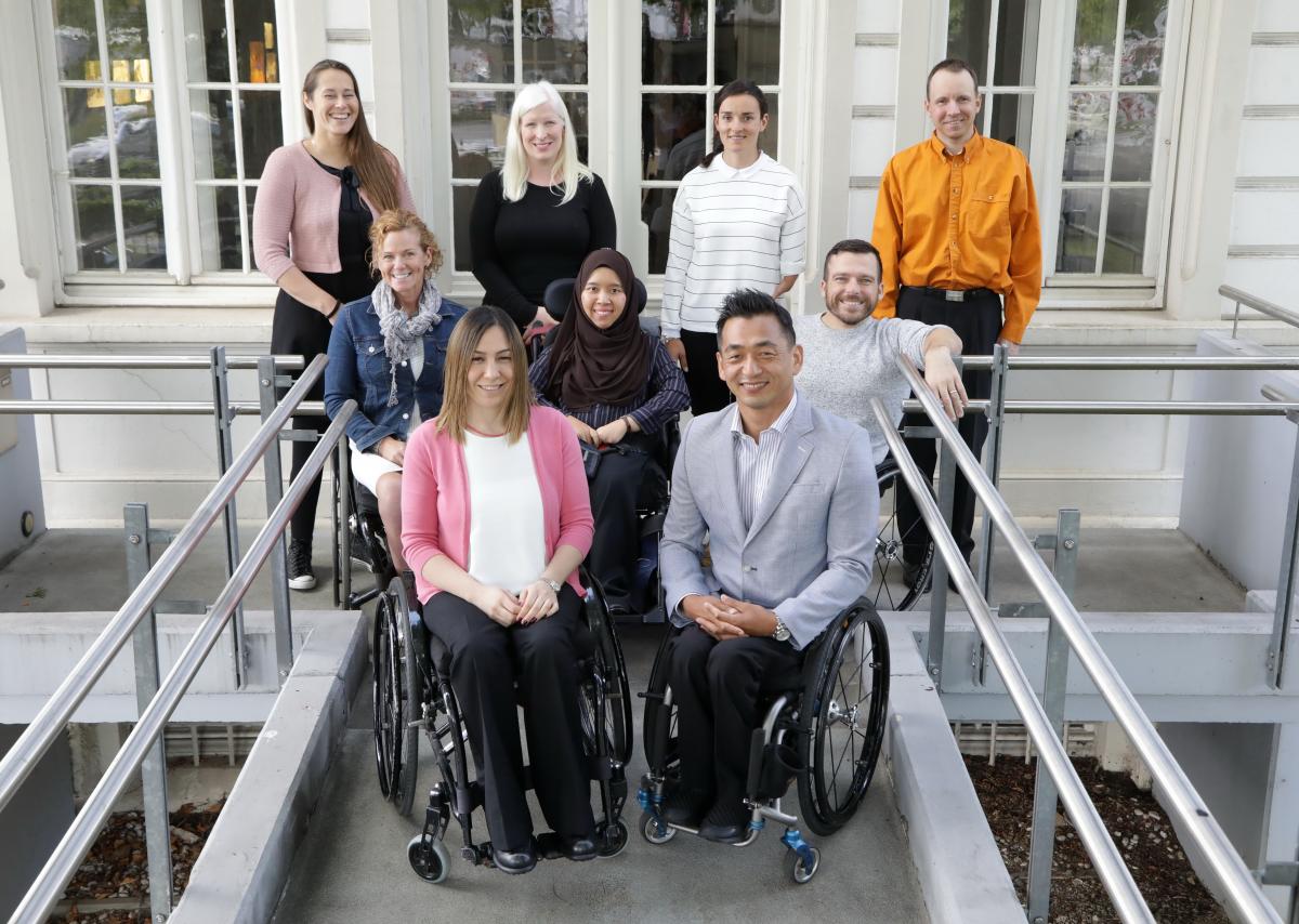 a group of male and female Para athletes sitting and standing outside a white building