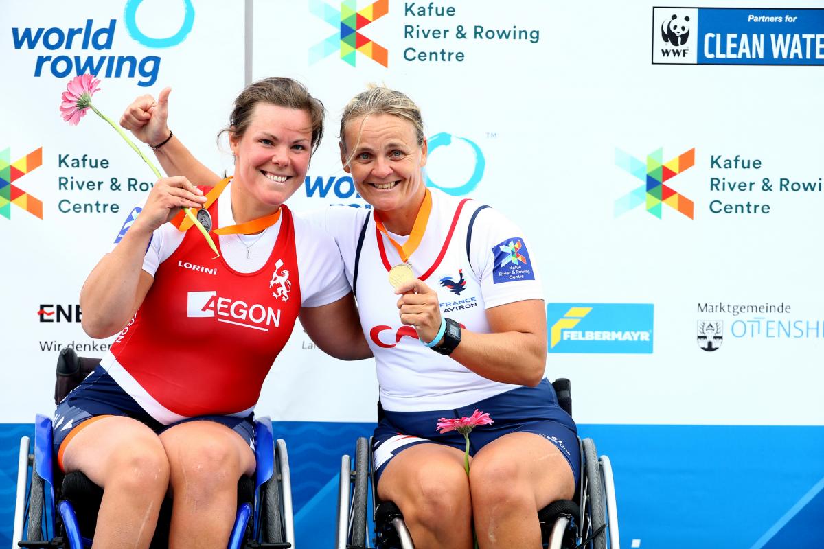 two female Para rowers in wheelchairs hug on the podium