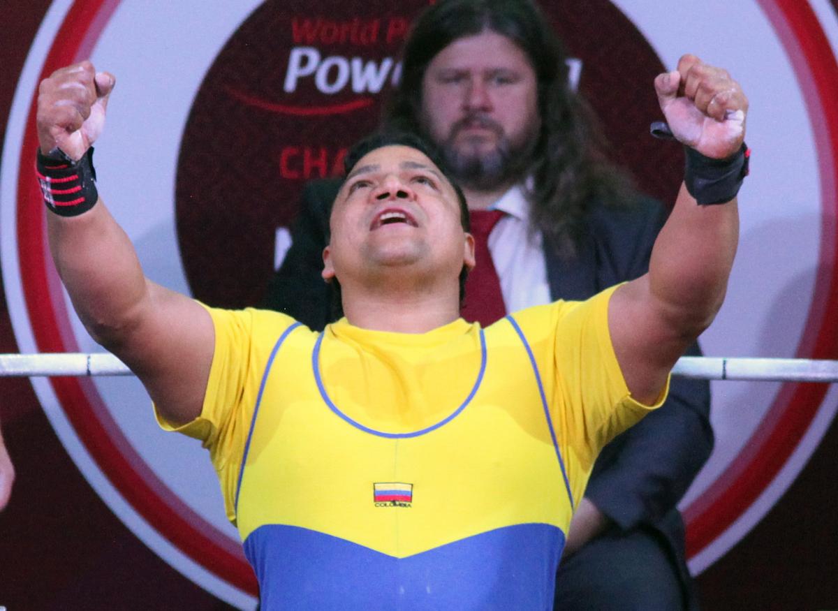 a male powerlifter raises his arms in celebration on the bench