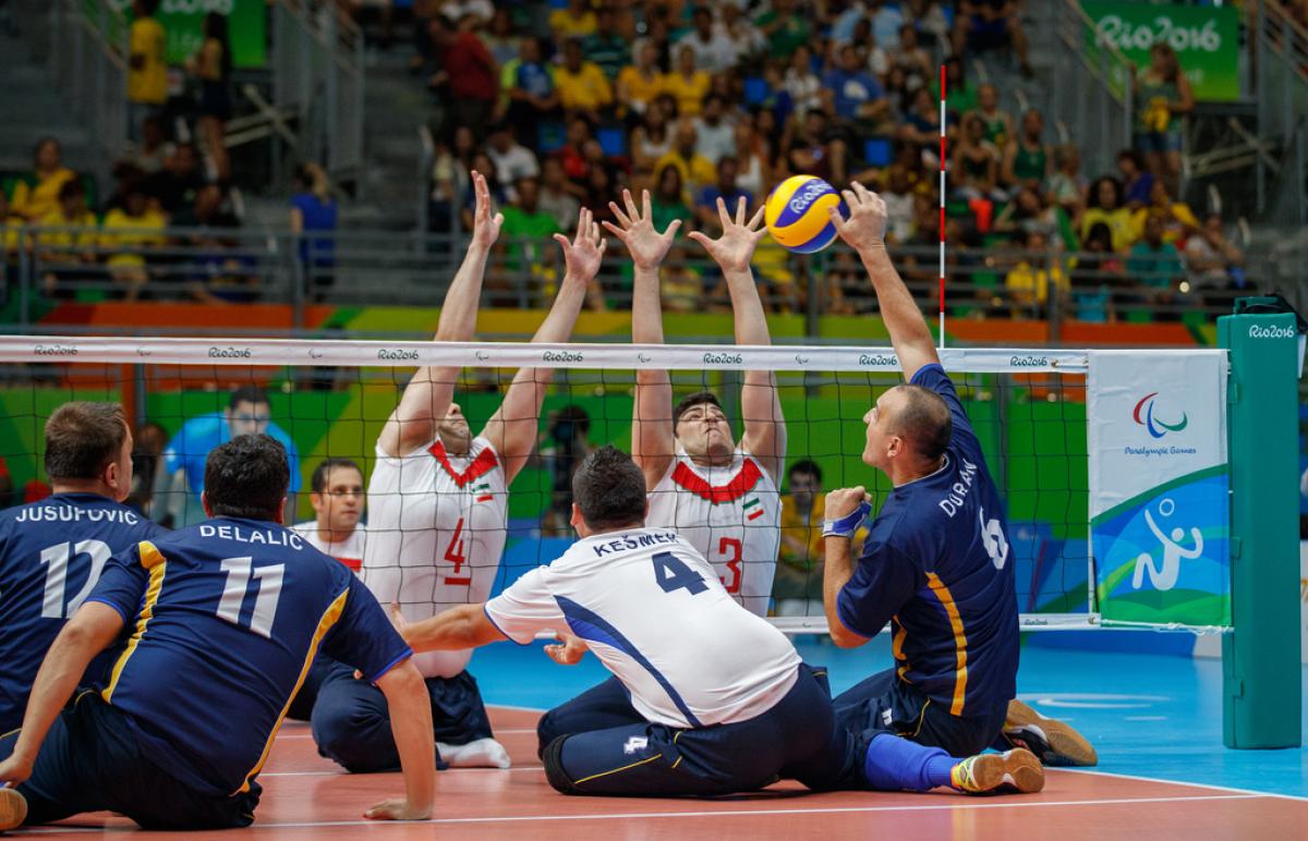 a group of male sitting volleyball players in action on the court