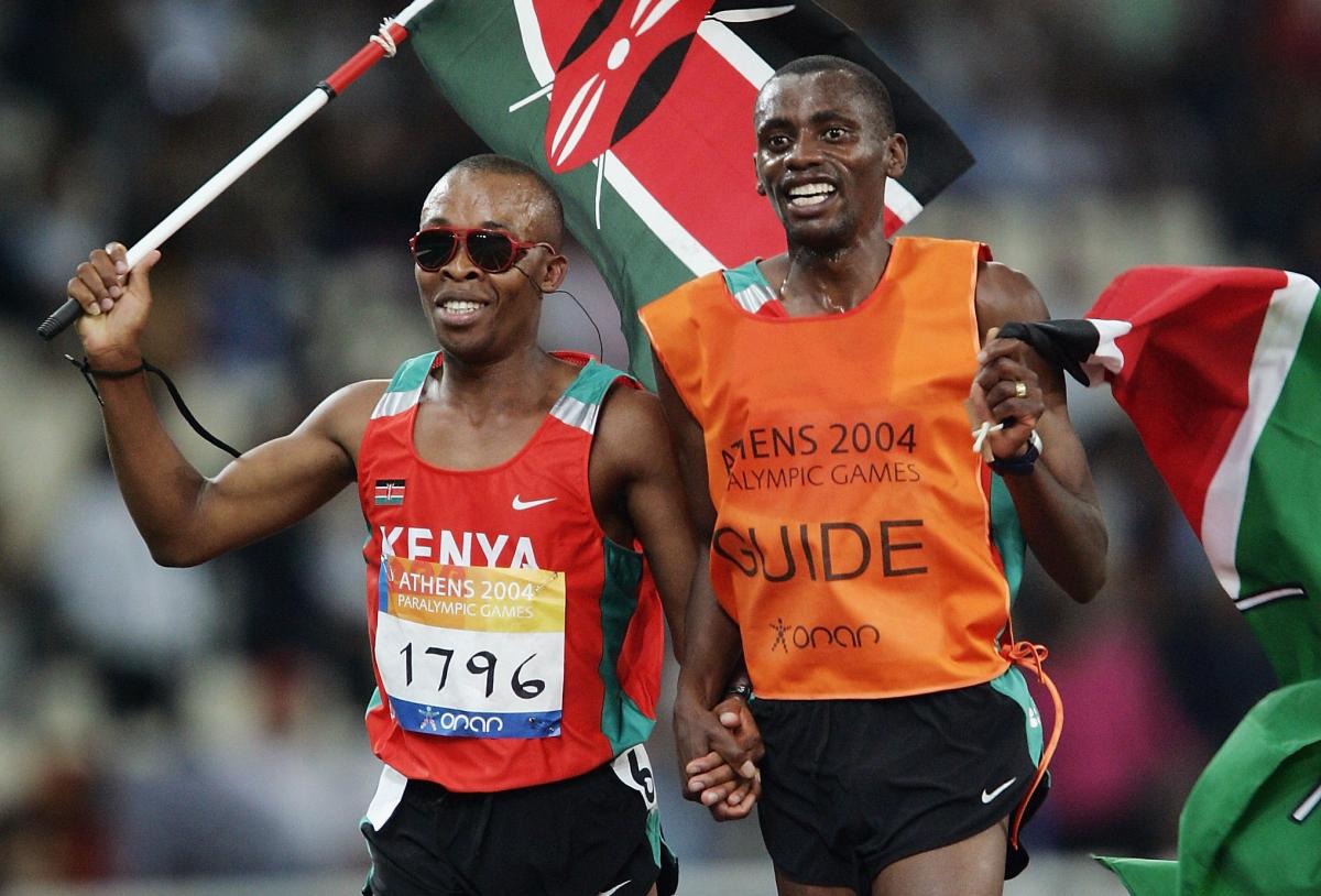 blind male runner Henry Wanyoike and his guide on a track carrying the Kenya flag