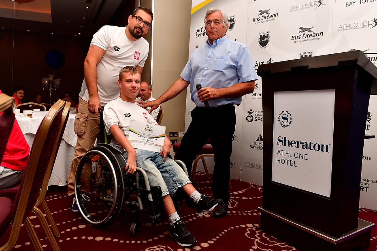Polish male swimmer Juliusz Trochimczuk in a wheelchair receives an award from two men
