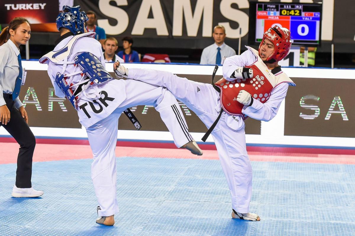 Two male taekwondo fighters kick each other