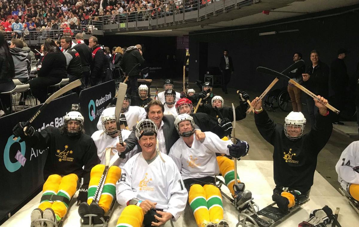 Fifteen people on sledges with Para ice hockey gear posing for a picture