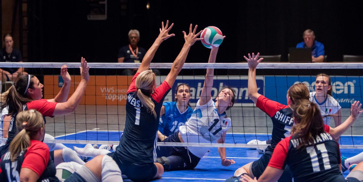 a group of female sitting volleyballers blocking the ball at the net 