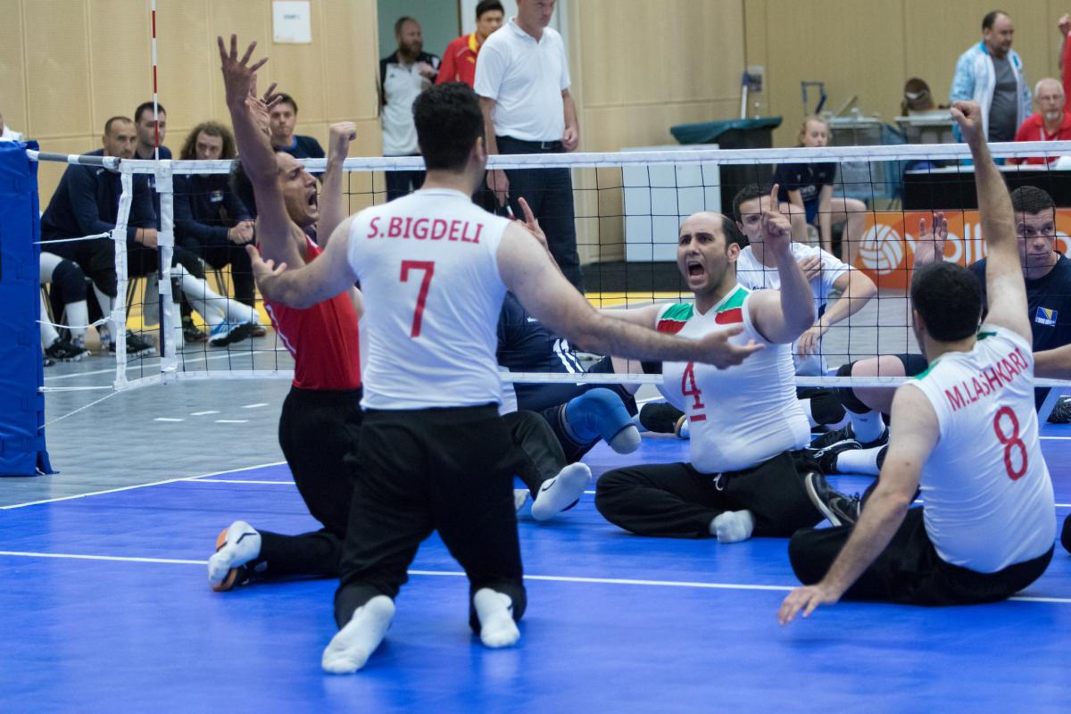 The Iranian men's sitting volleyball team throw their arms up in celebration on the court