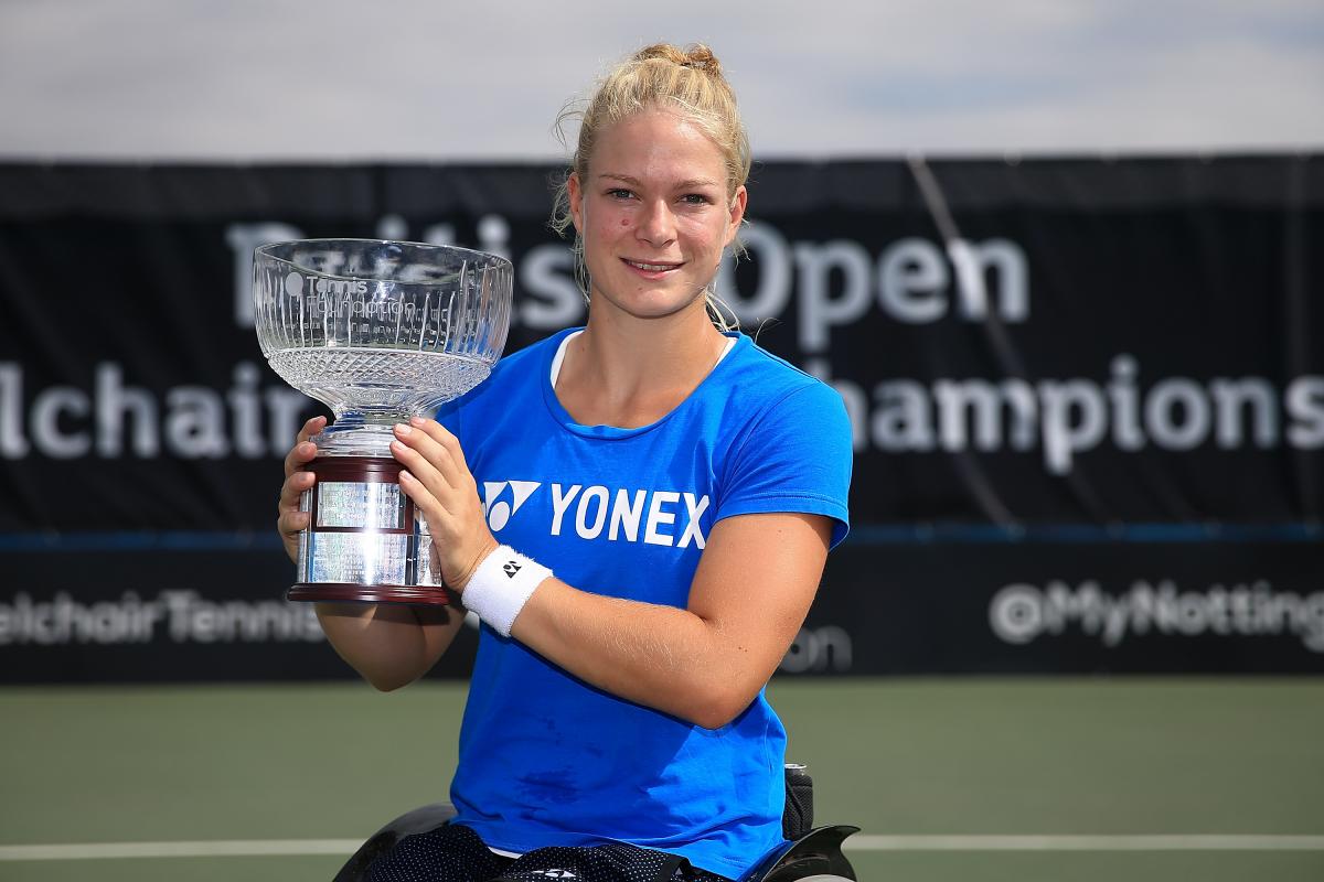 Female wheelchair tennis player Diede de Groot smiles and lifts a glass trophy