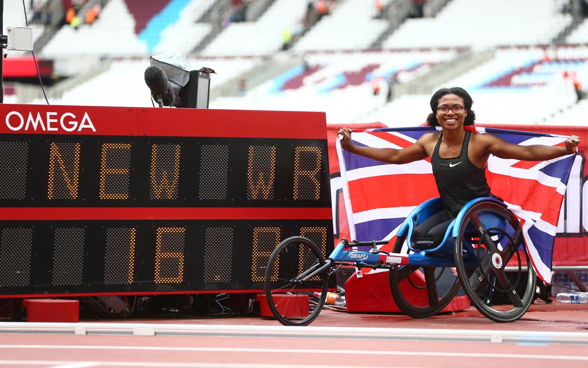 Female wheelchair racer Kare Adenegan holds up a British flag next to the display of her world record time
