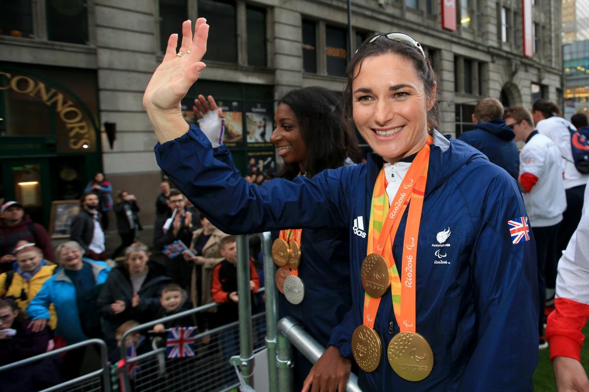 female Para cyclist Sarah Storey waves to fans from the top of a bus 