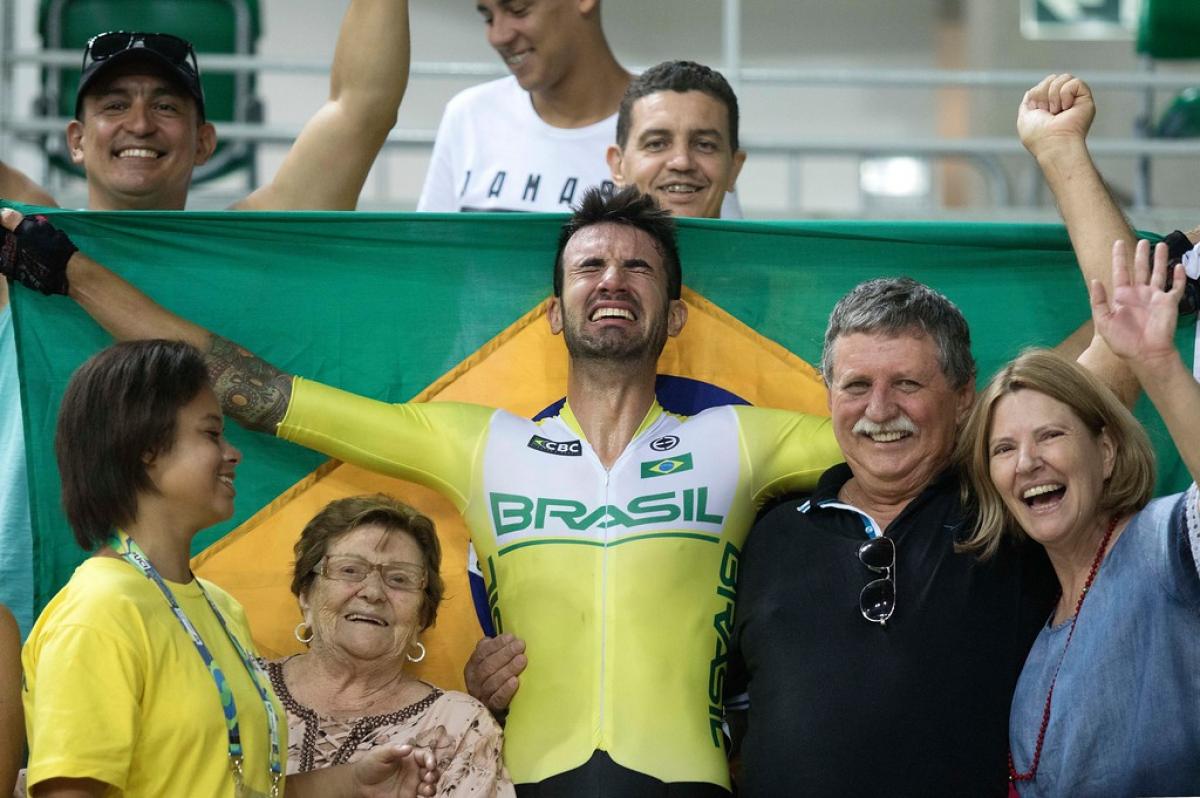 male Para cyclist Lauro Chaman celebrates with his family and holds up the Brazil flag