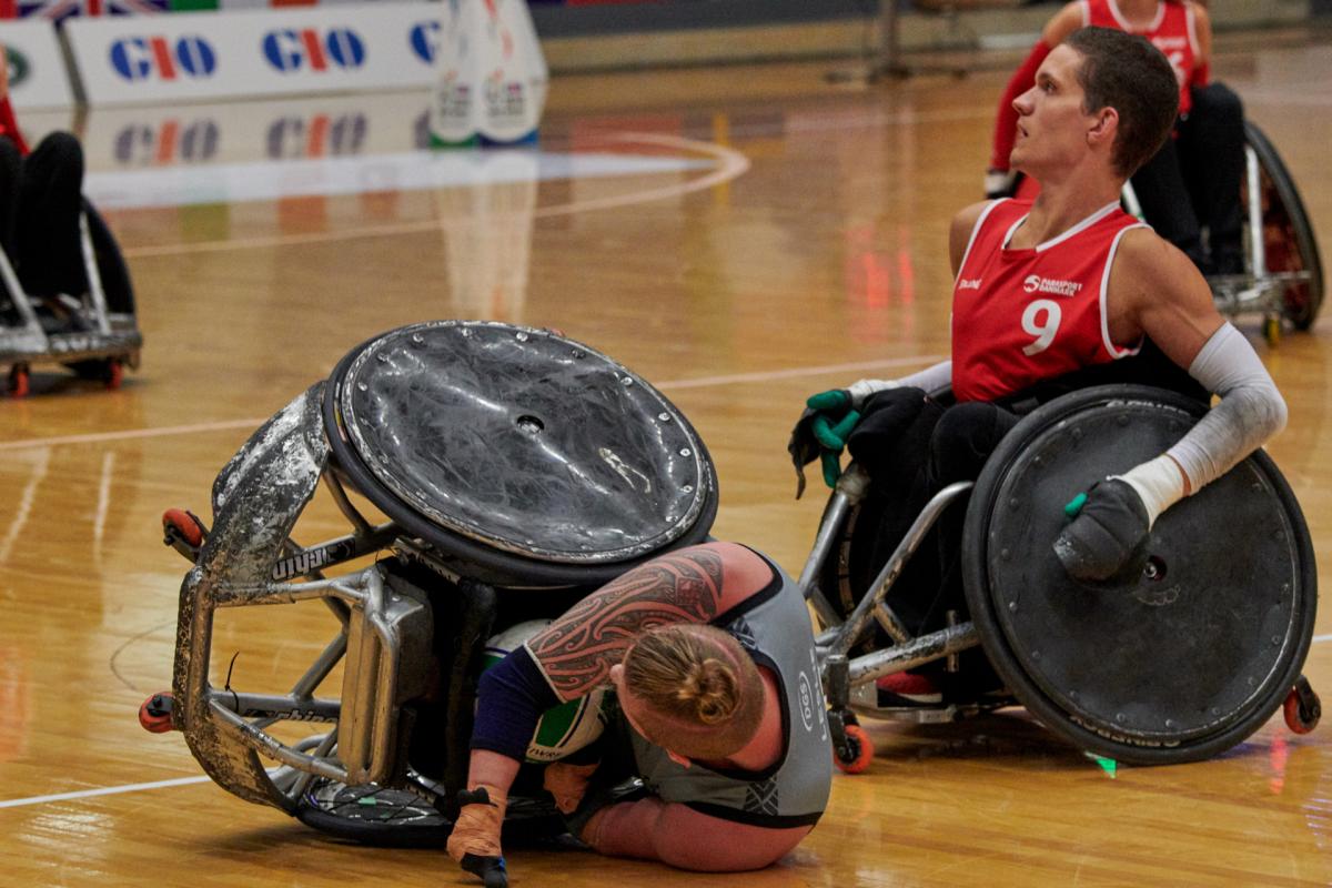 a Danish wheelchair rugby player on the ground after a tackle from a New Zealand wheelchair rugby player