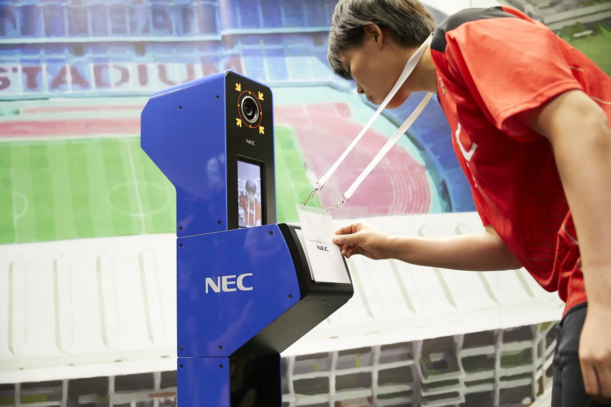 a person looks into a camera while displaying their accreditation in a simulation of the Tokyo 2020 system