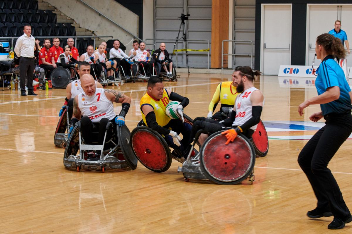 two Colombian wheelchair rugby players tackling a Polish player for the ball