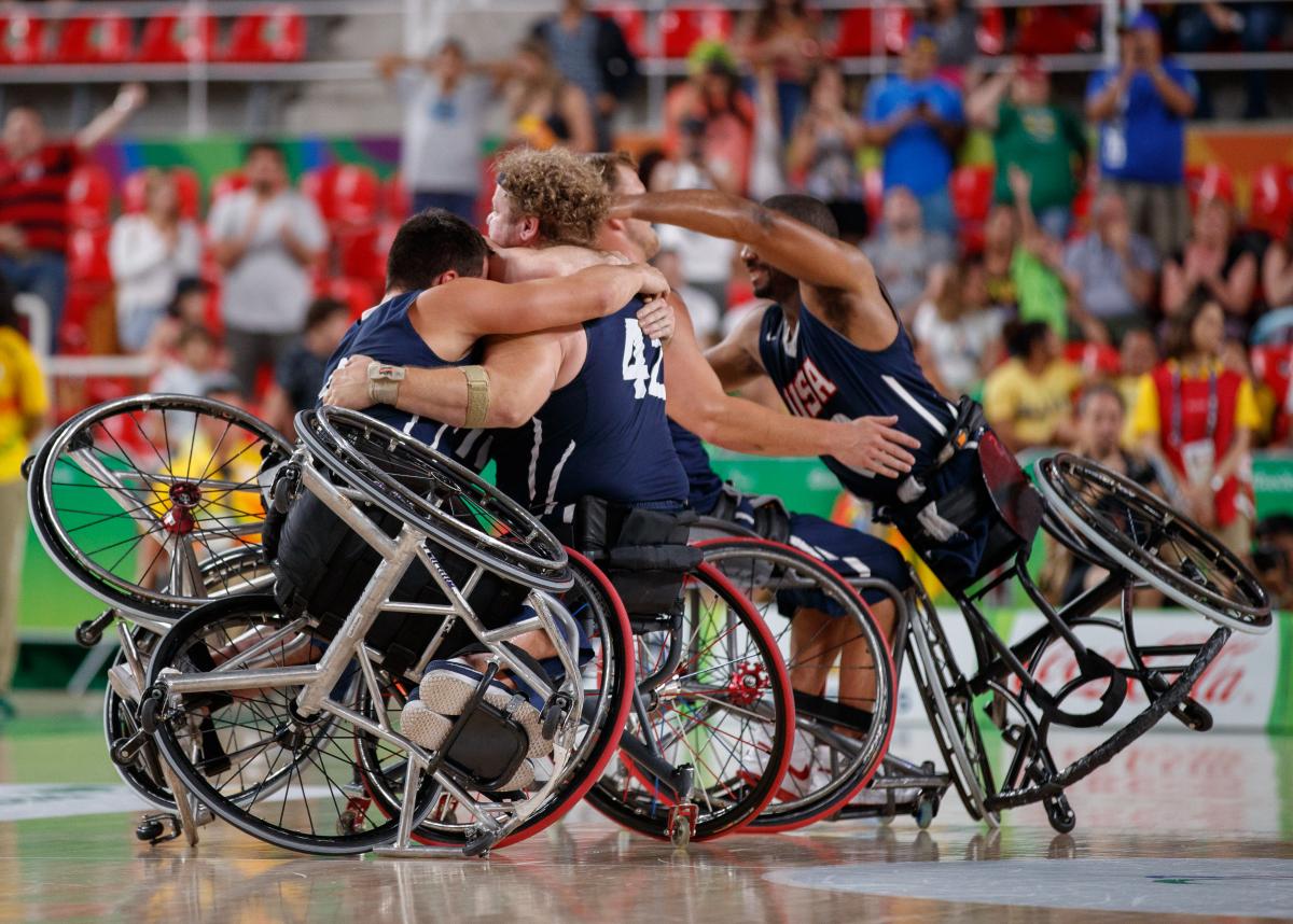 a group of male wheelchair basketballers from the USA hug on the court