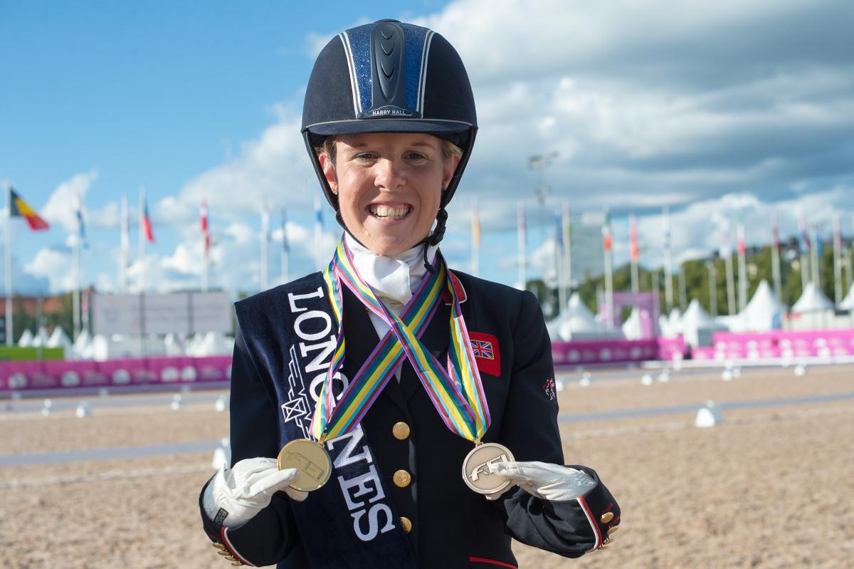 female Para equestrian rider Erin Orford smiles and holds up two gold medals around her neck