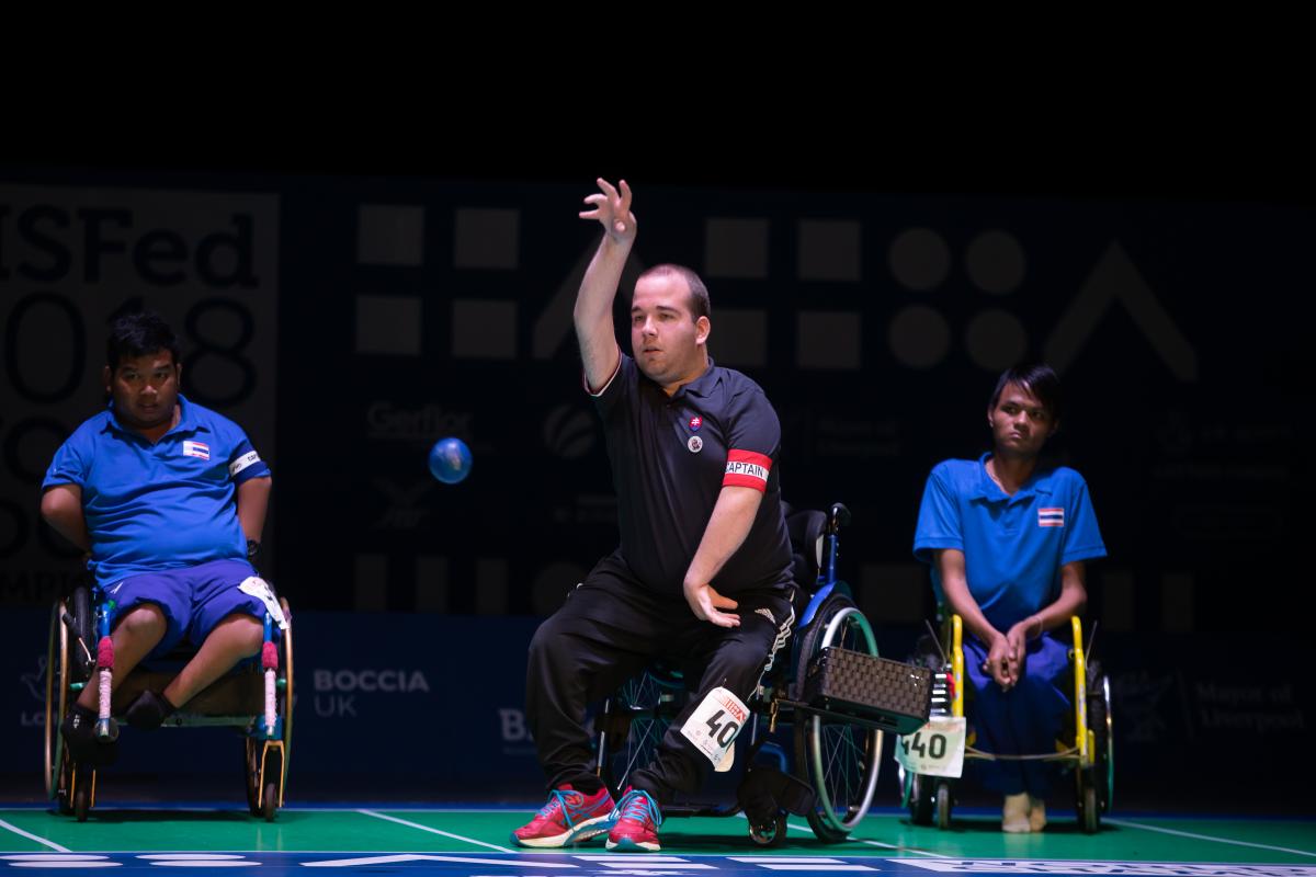 Men in a wheelchair throwing a blue ball observed by other two men