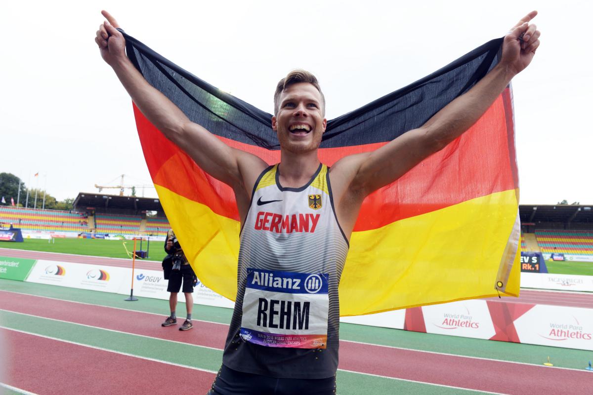 male long jumper Markus Rehm holding up the Germany flag and smiling