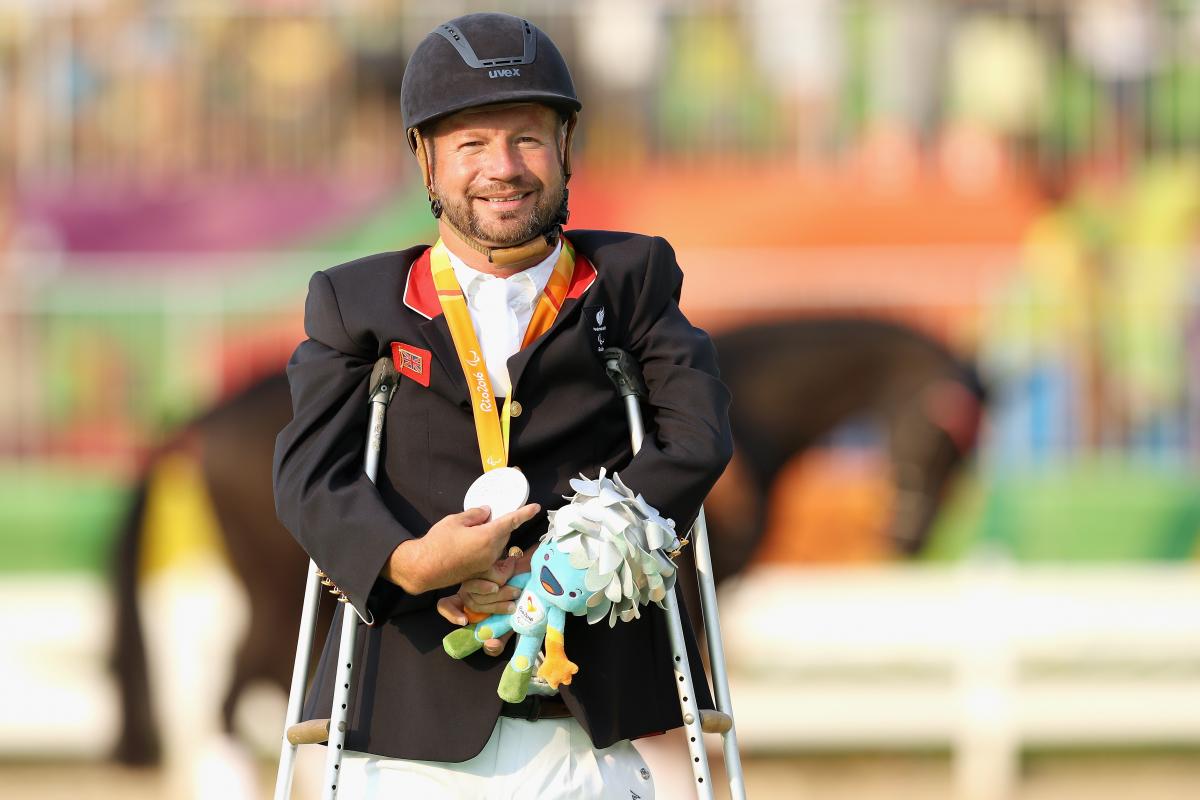male Para equestrian rider Lee Pearson standing on crutches holding a medal
