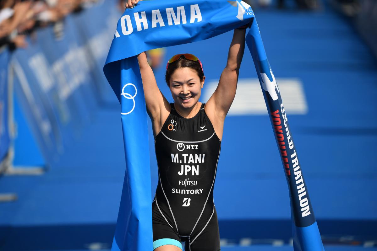 female Para triathlete Mami Tani holds up the finish tape as she crosses the line