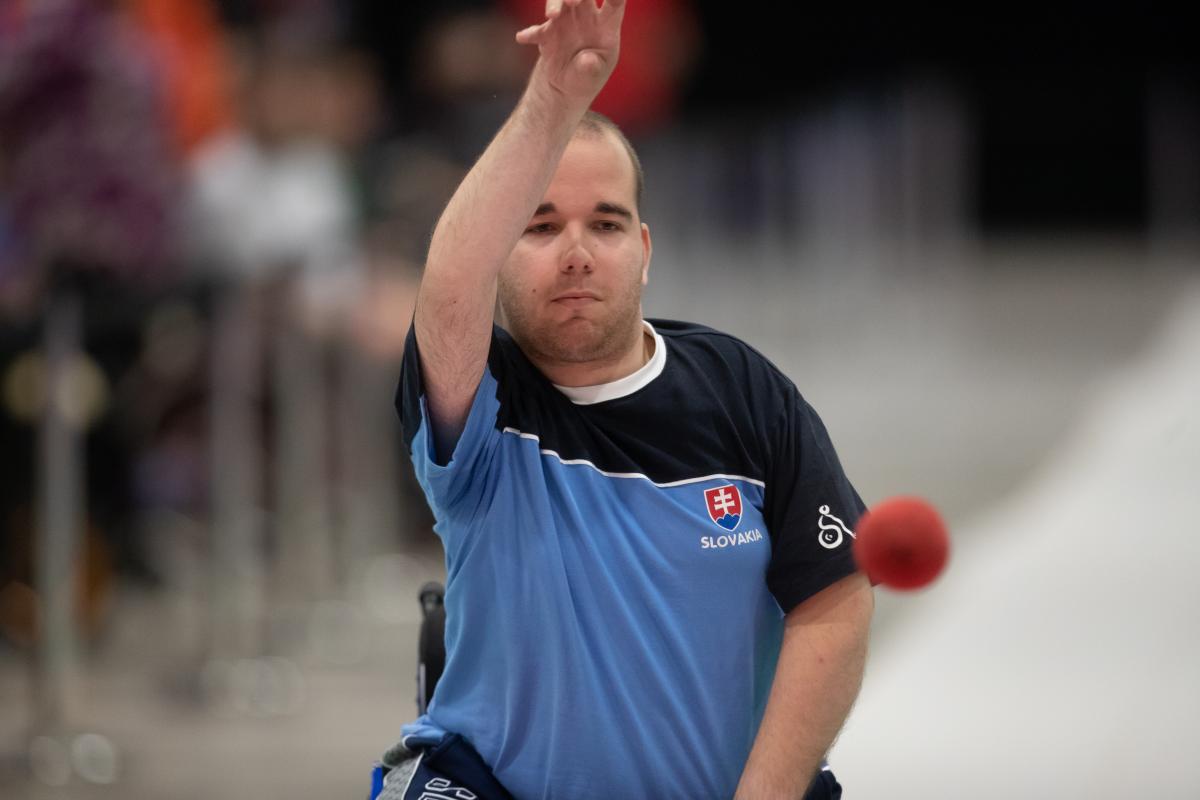 Male boccia player throws red ball