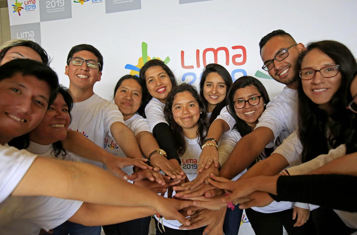 Lima 2019 volunteers programme Twelve people smiling and placing their hands on each others'
