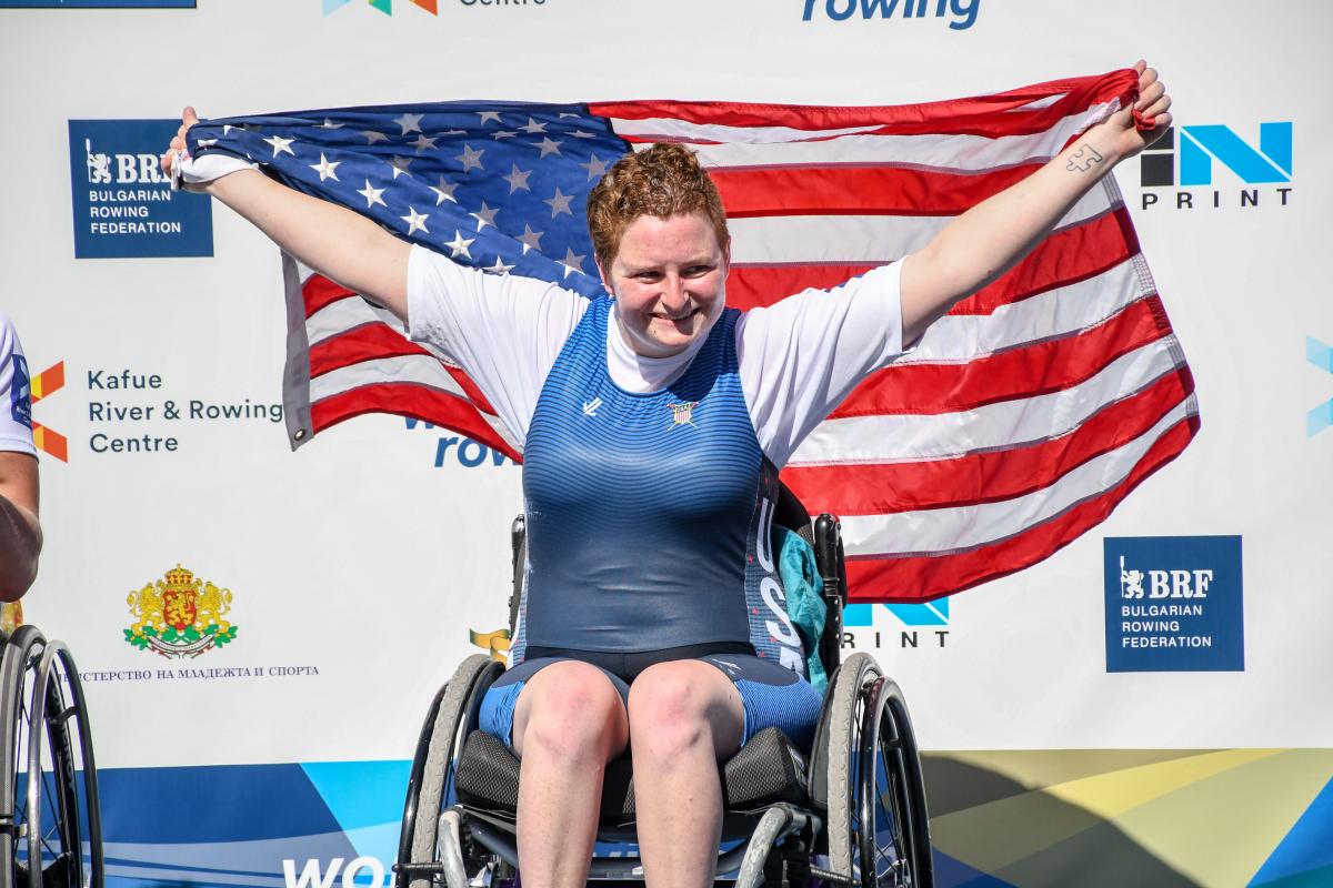 female Para rower Hallie Smith smiling and holding up a USA flag