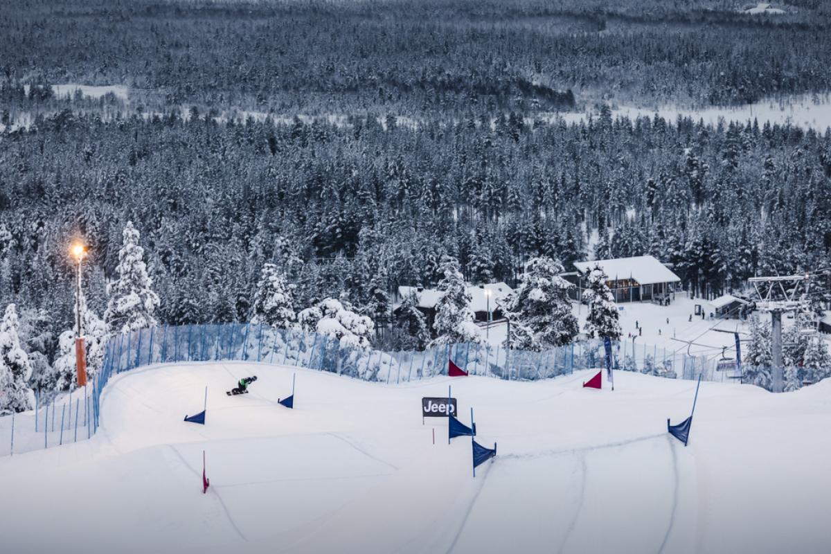 a wide shot of a snowboarder riding a course with snow-covered trees in the background