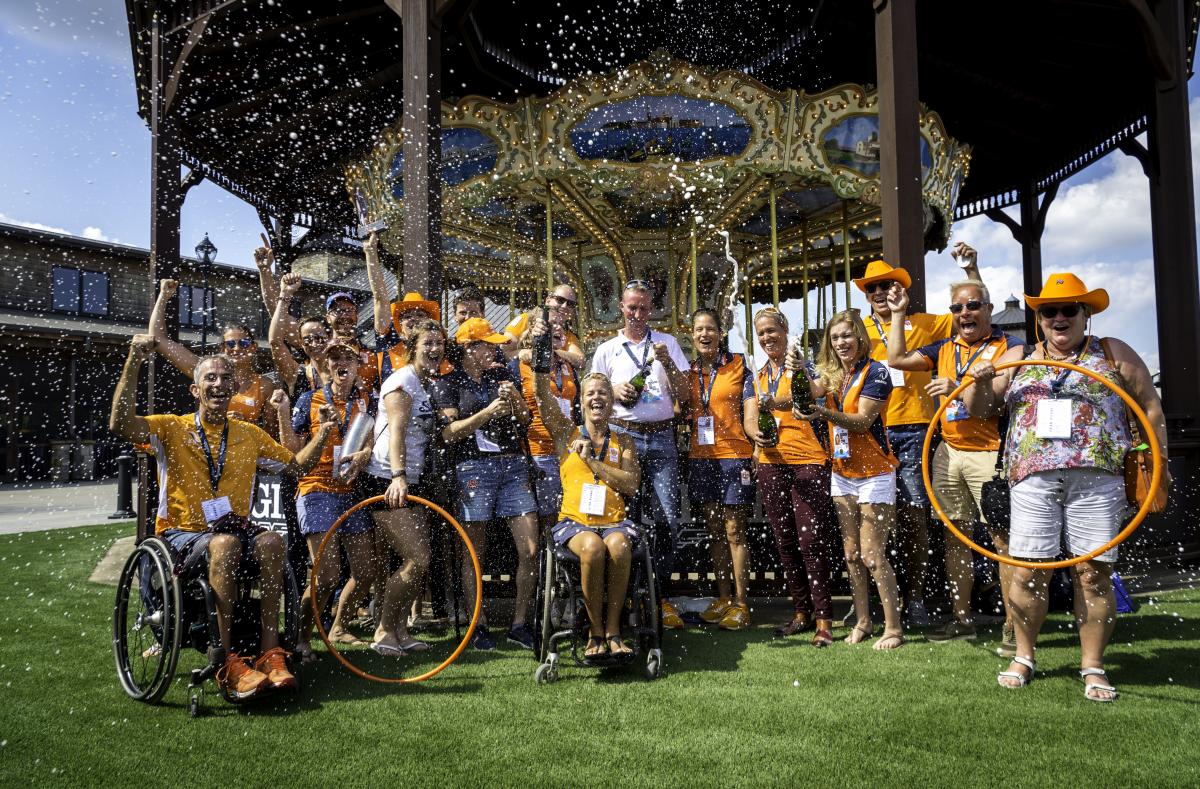 Group photo of Dutch Para equestrian team dressed in orange team colors celebrating with champagne