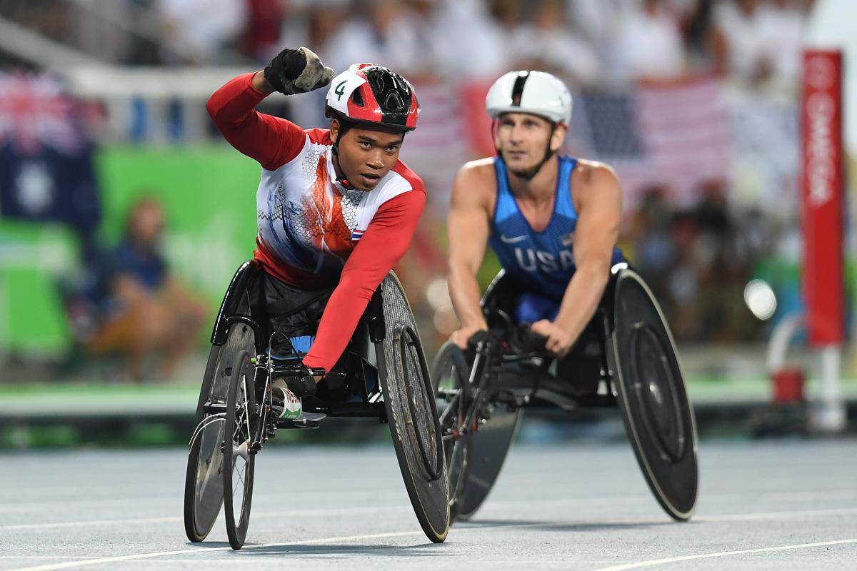 Man in a race wheelchair celebrating with another man in a race wheelchair behind him
