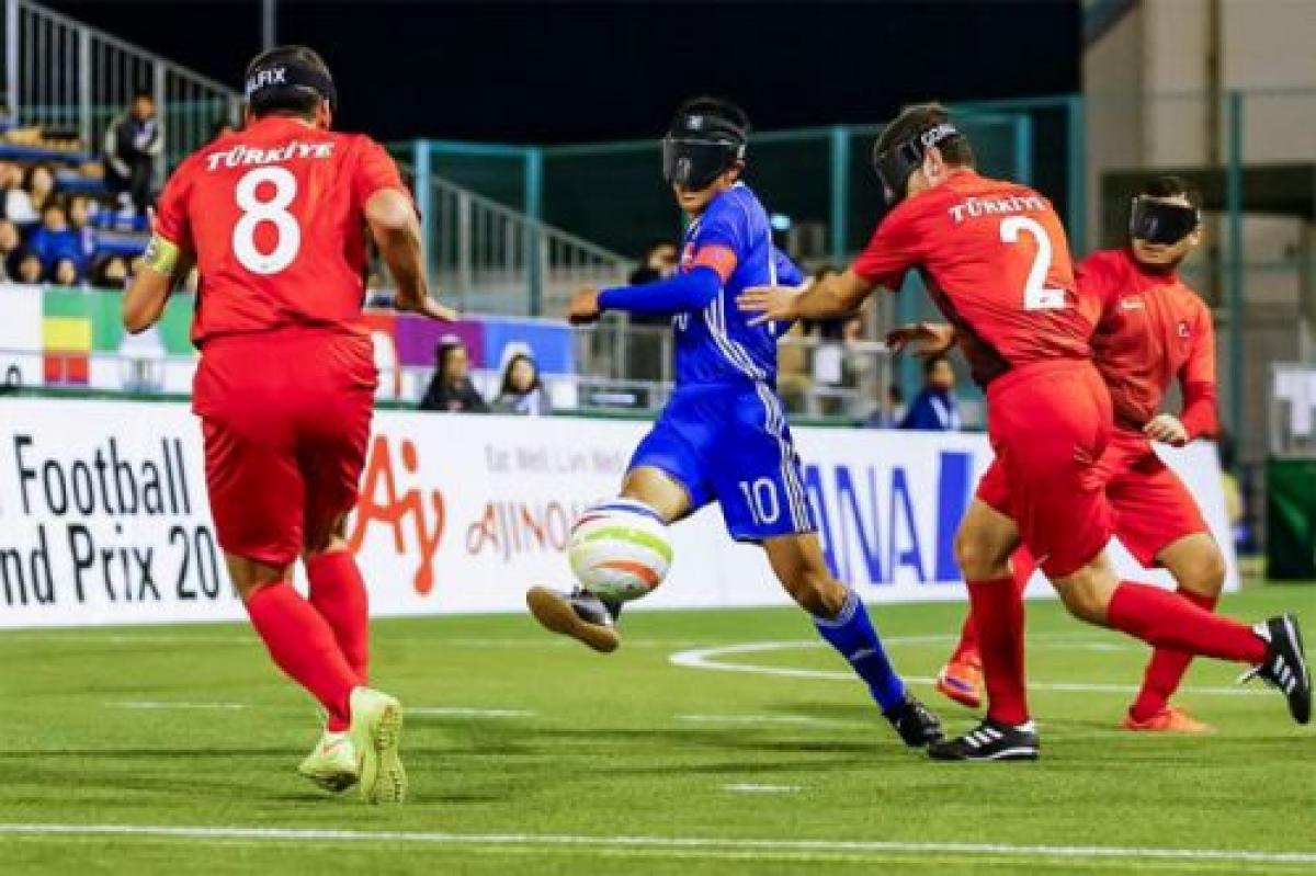 a Japanese blind footballer dribbles the ball through two opponents