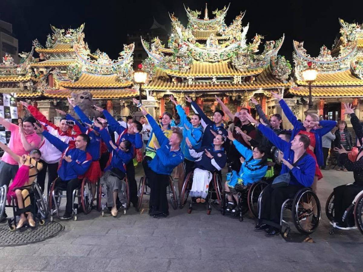 a group of Para dancers raising their arms in front of three golden Chinese temples