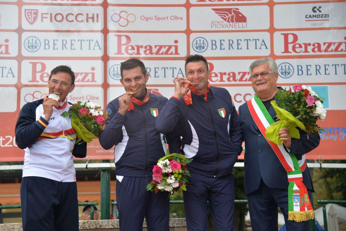 three male Para shooters with Francesco Nespeca in the middle, biting their medals