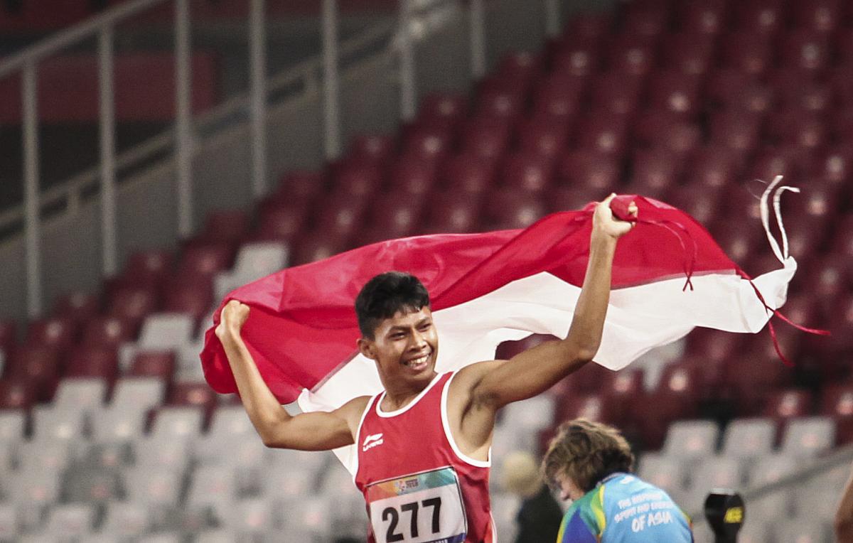male Para athlete Sapto Yogo Purnomo running holding an Indonesia flag