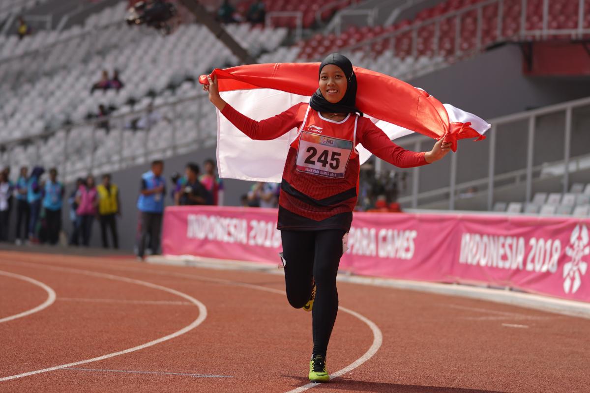 Karisma Tiarani - Indonesia 2018 female Para athlete Karisma Tiarani runs down the track holding an Indonesia flag
