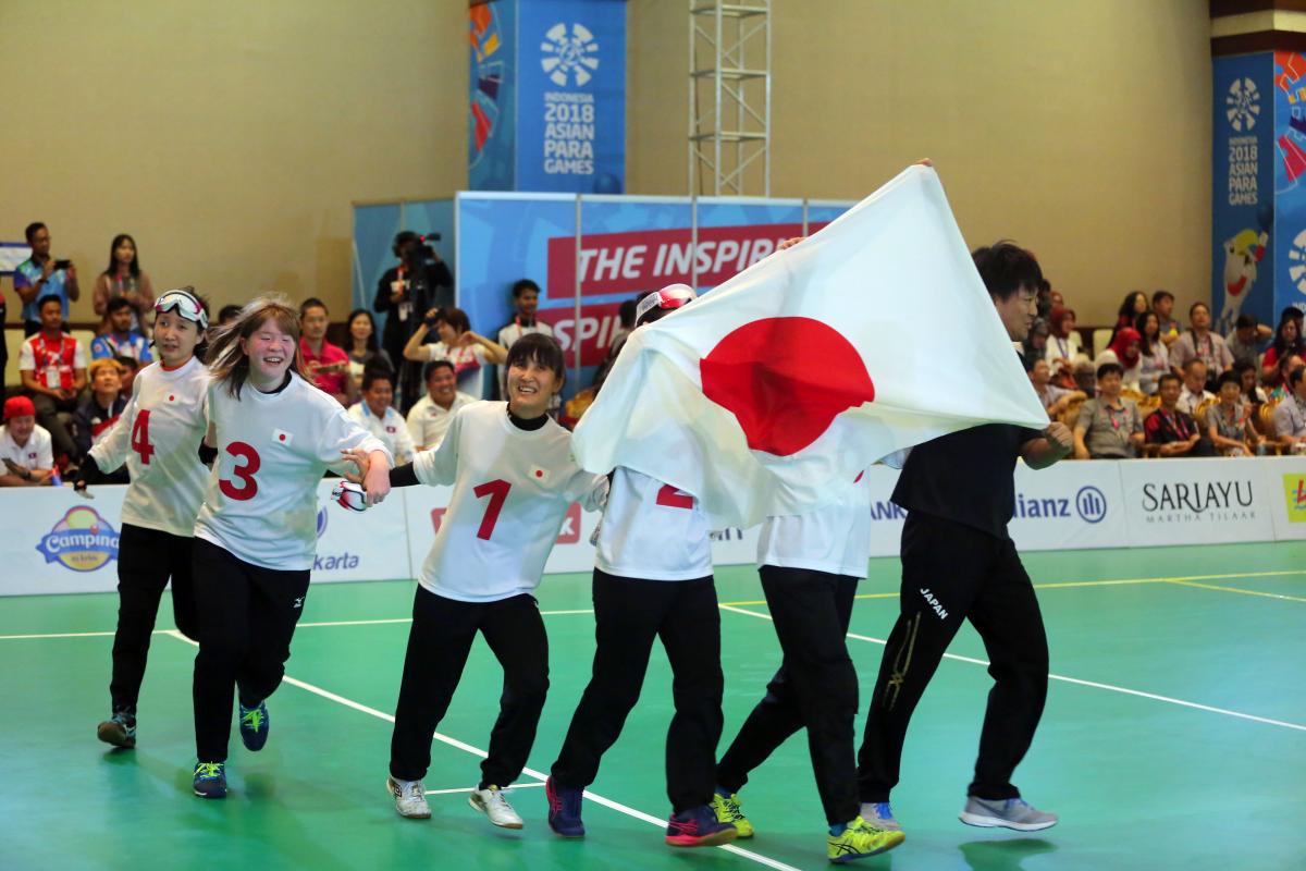 Japan women's goalball - Indonesia 2018 Japanese female goalball players run across the court holding a Japan flag