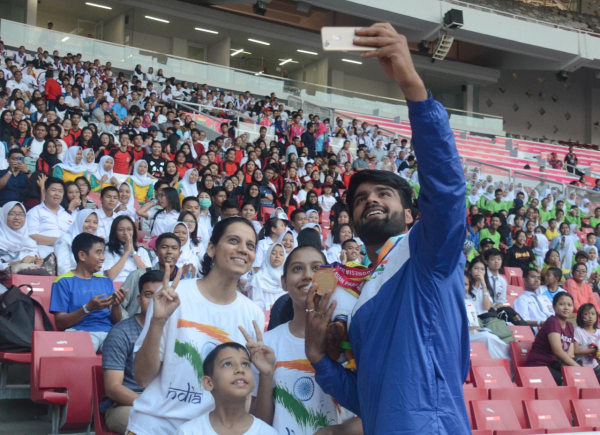 Man with a medal taking pictures with fans on the stands in a stadium