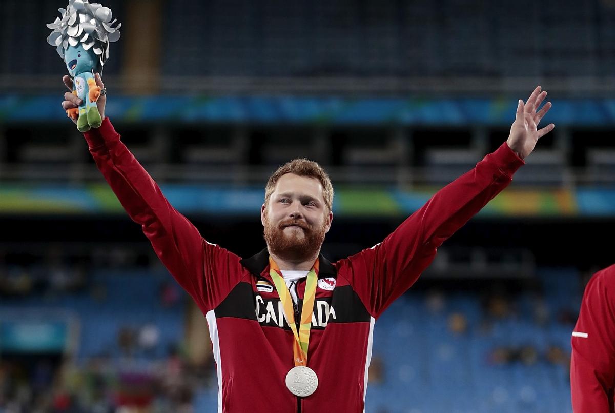 male Para athlete Alister McQueen raises his arms on the podium